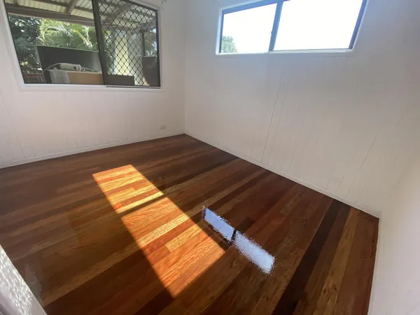 Sunlight across polished brown floorboards in a white bedroom
