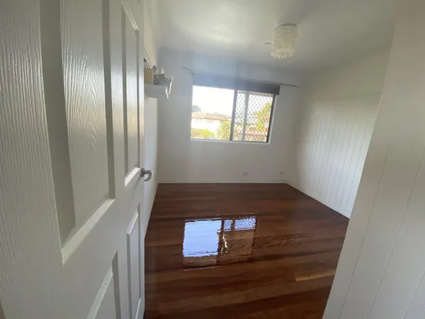 Polished bedroom floor beneath a window in a white panelled wall