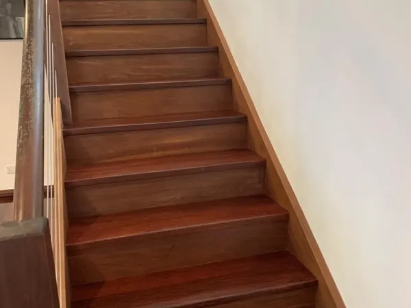 Finished timber stairs rising between white walls and a wooden handrail