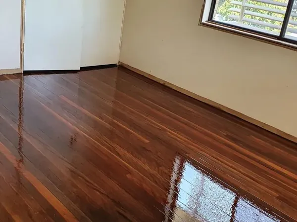 Glossy dark floorboards in a room with white walls and a screened window
