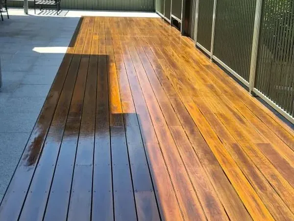 Long outdoor timber deck with a reflective finish beside a garden fence