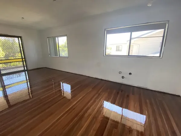 Reflective timber floor in an empty living room with windows on two walls