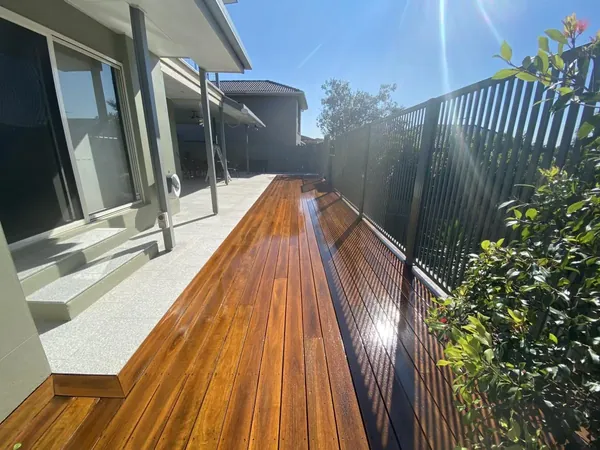 Freshly finished outdoor timber deck beside sliding doors and a black fence