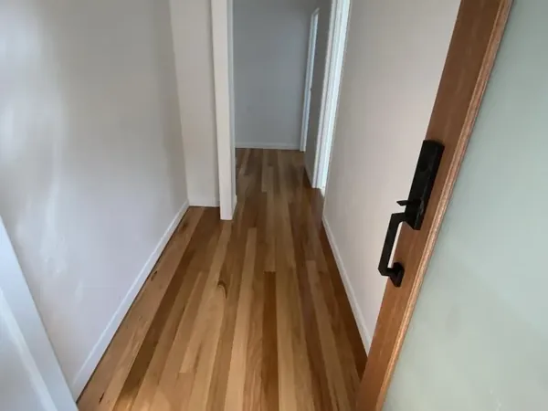 Light timber floorboards running along a narrow white hallway