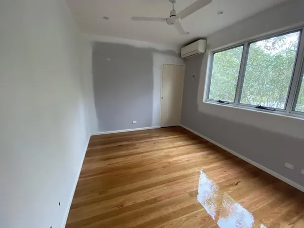 Glossy timber floor in a bright bedroom with large windows and a ceiling fan