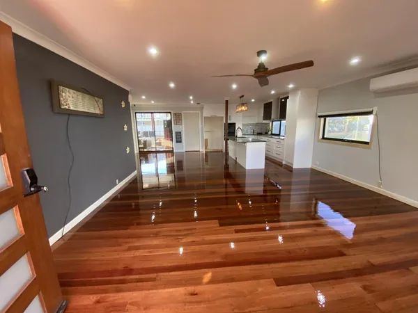 Glossy timber floor through a large open living area with a white kitchen
