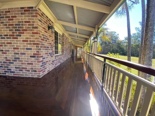 Covered timber veranda with a reflective finish beside an exposed brick wall