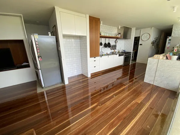 Warm timber flooring beneath a white kitchen with a breakfast bench