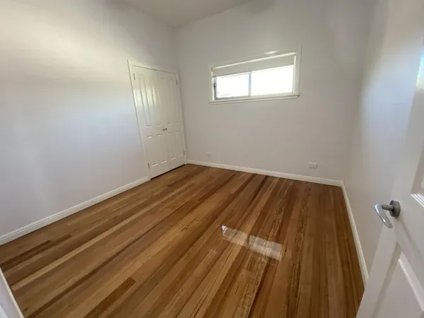 Light finished timber floor in a bedroom with white walls and a high window