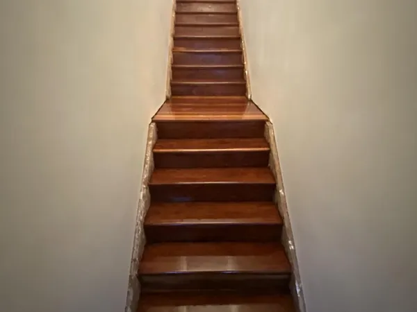 Dark finished timber staircase rising between white walls