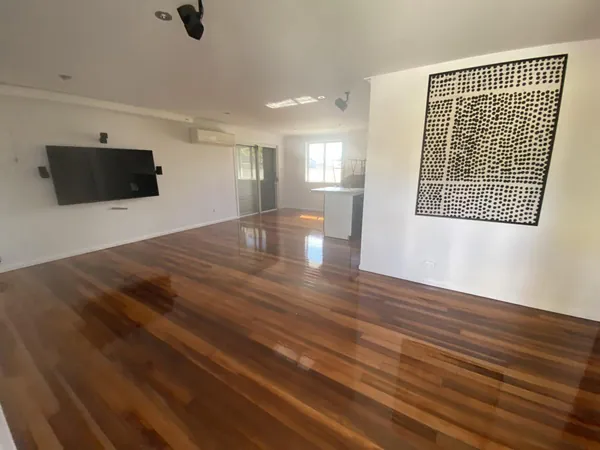 Glossy timber floor through a spacious living room with a wall-mounted television
