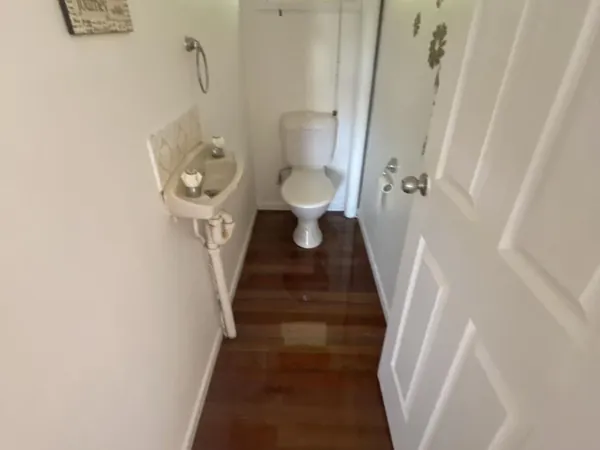 Polished timber floor in a narrow toilet room with a small hand basin