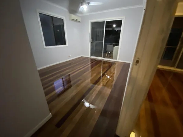 Reflective timber floor beside a white kitchen and an adjoining grey-walled room