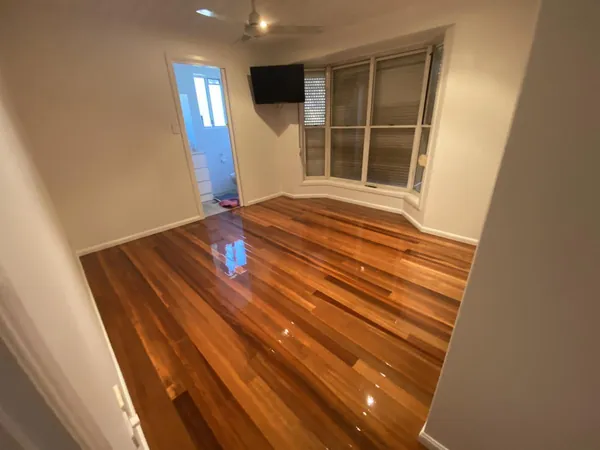Glossy reddish floorboards in an empty room with a bay window