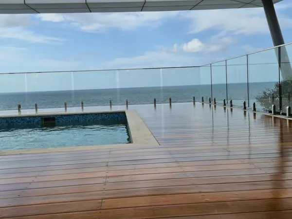 Finished timber decking surrounding a pool with a glass safety fence