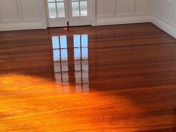 Sunlight reflecting on reddish polished floorboards beside white panelled walls