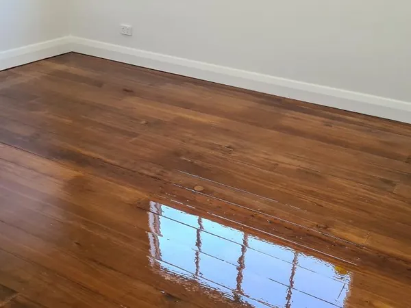 Reflective brown floorboards along a white wall with skirting boards