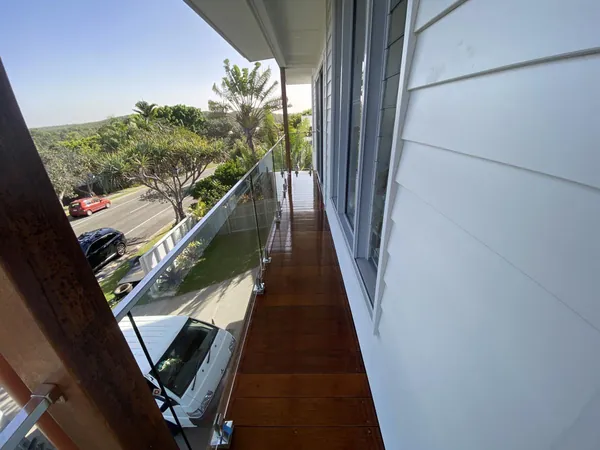 Narrow polished timber balcony beside white weatherboards and a metal railing