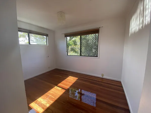 Sunlit polished timber floor in a bedroom with a large screened window