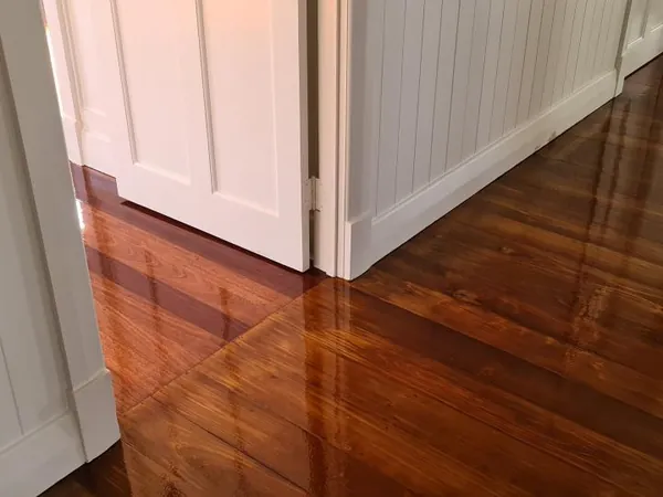Dark glossy floorboards connecting two rooms with white panelled walls