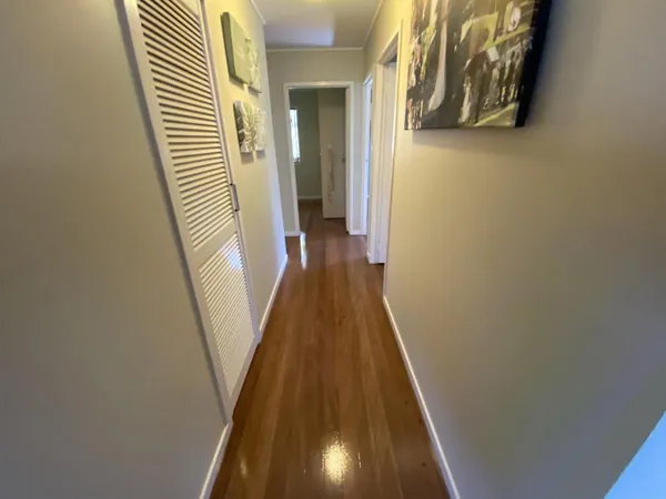 Polished timber floor in a hallway with framed artwork and louvred doors