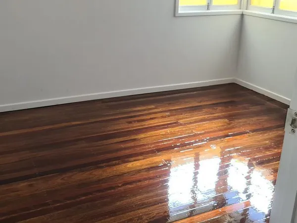 Dark polished floorboards in an empty room with a large window