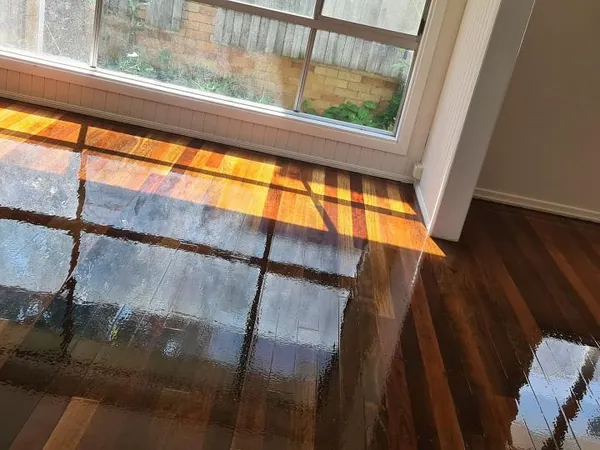 Dark glossy floorboards beside glass doors and an exposed brick wall